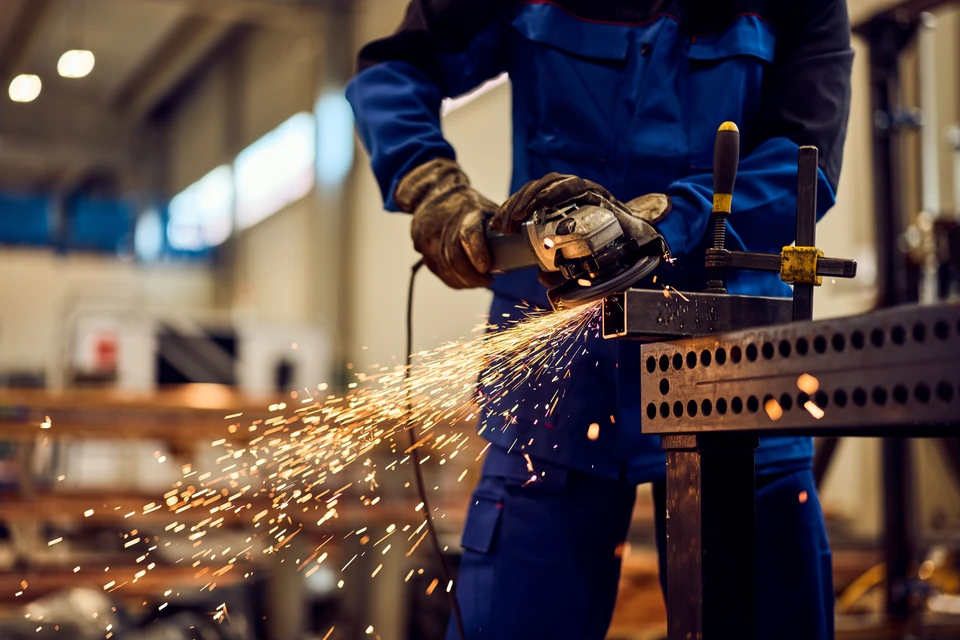 Ouvrier soudeur en combinaison bleue et rouge travaillant sur une structure métallique à l'extérieur